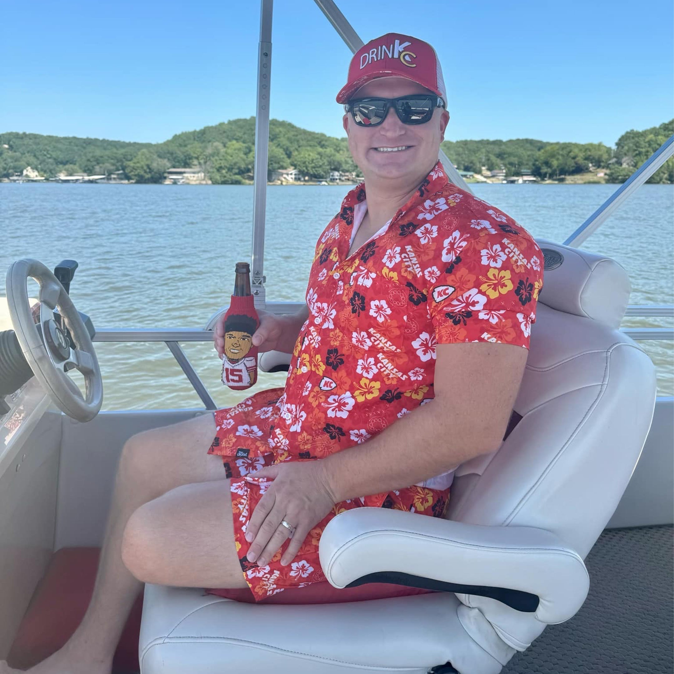 Person on a boat wearing a red floral dress and sunglasses, holding a bottle.