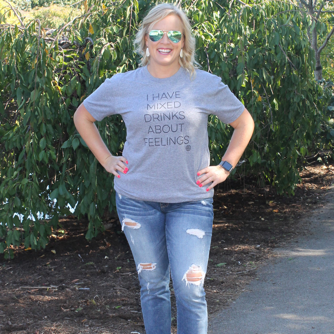 Woman wearing a gray t-shirt with text and ripped jeans standing outdoors.