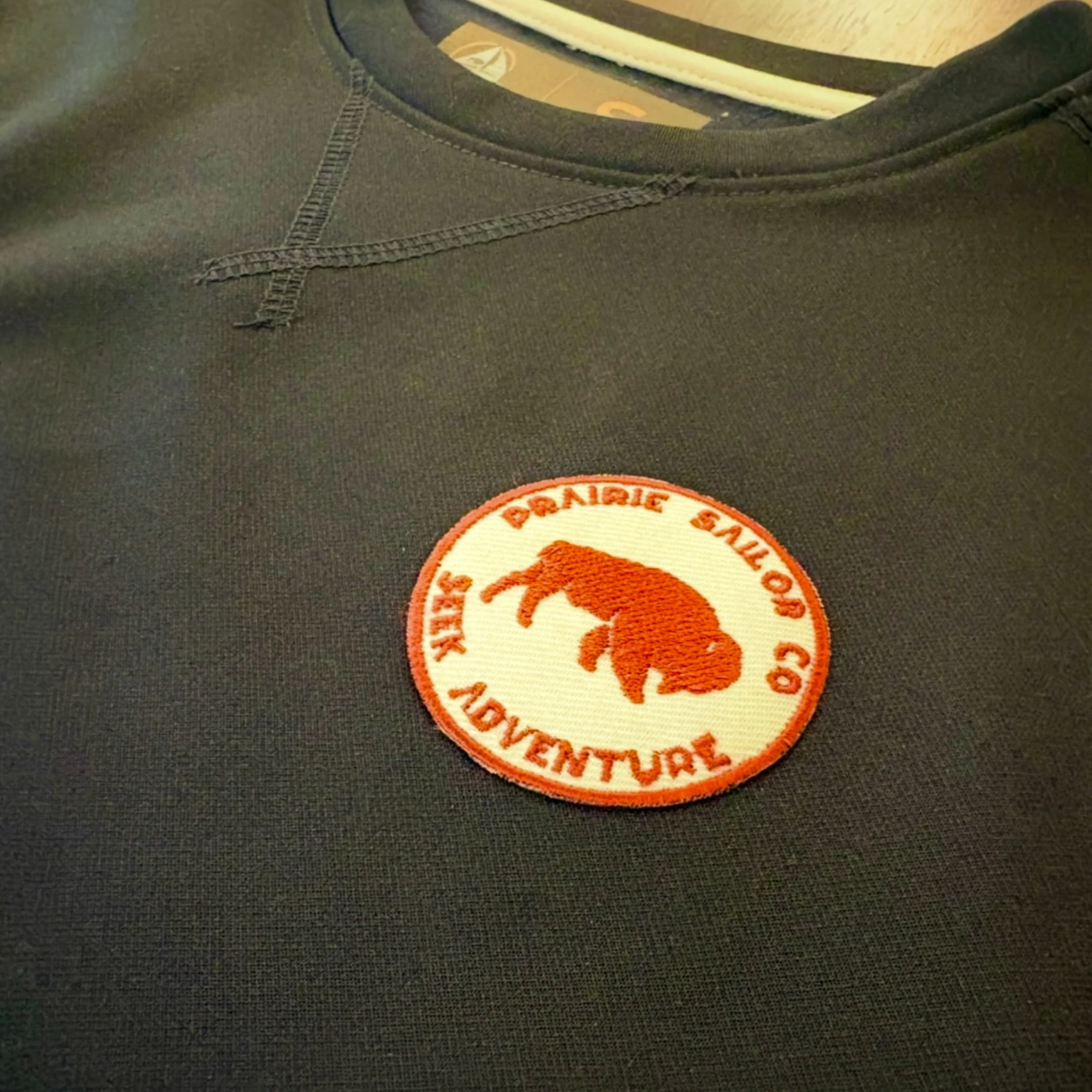 Dark green sweatshirt with a red and white patch featuring text and an animal illustration.