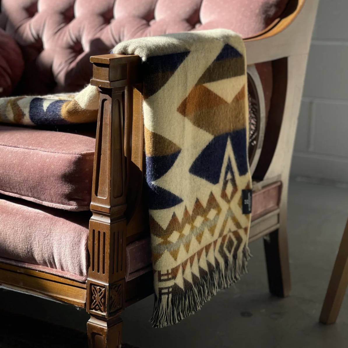 Patterned blanket draped over a wooden armchair with a blurred background