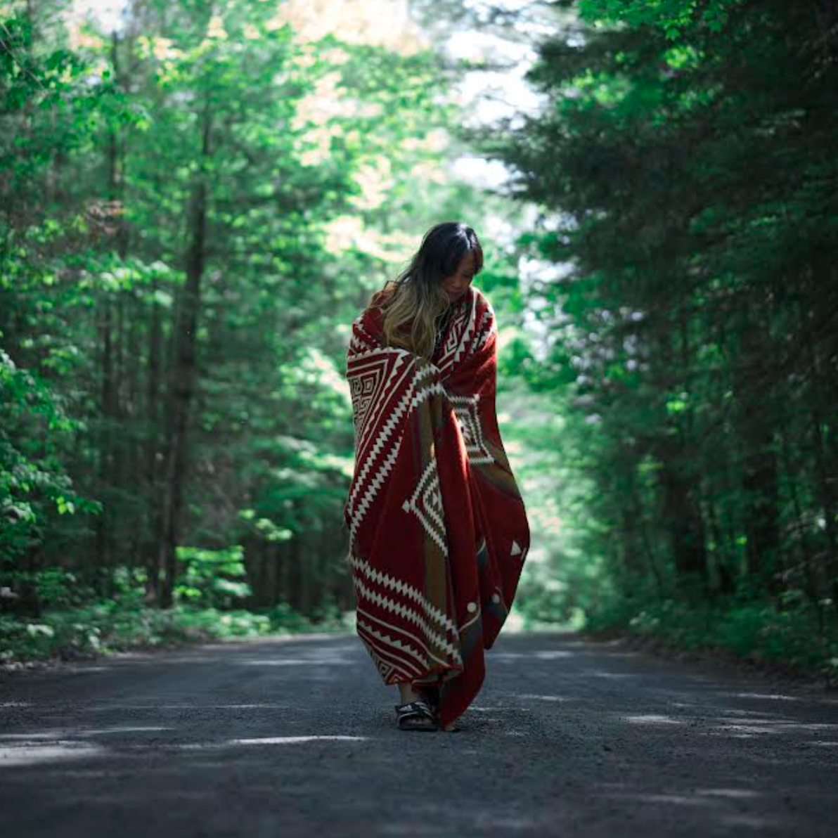 Person walking on a path in a forest with a red and white patterned blanket wrapped around them