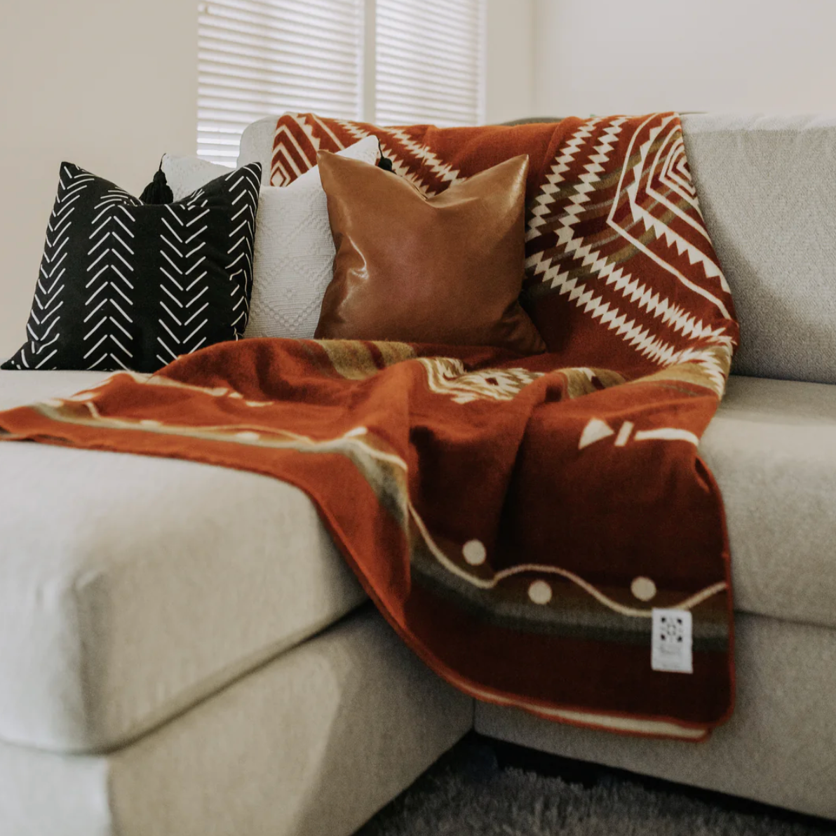Decorative throw blanket with geometric pattern draped over a sofa with pillows.