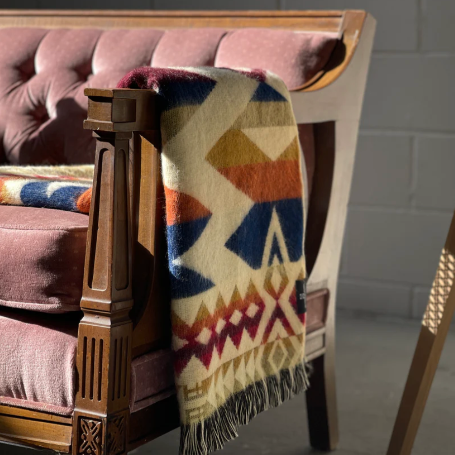 Colorful patterned blanket draped over a wooden armchair with a brick wall background