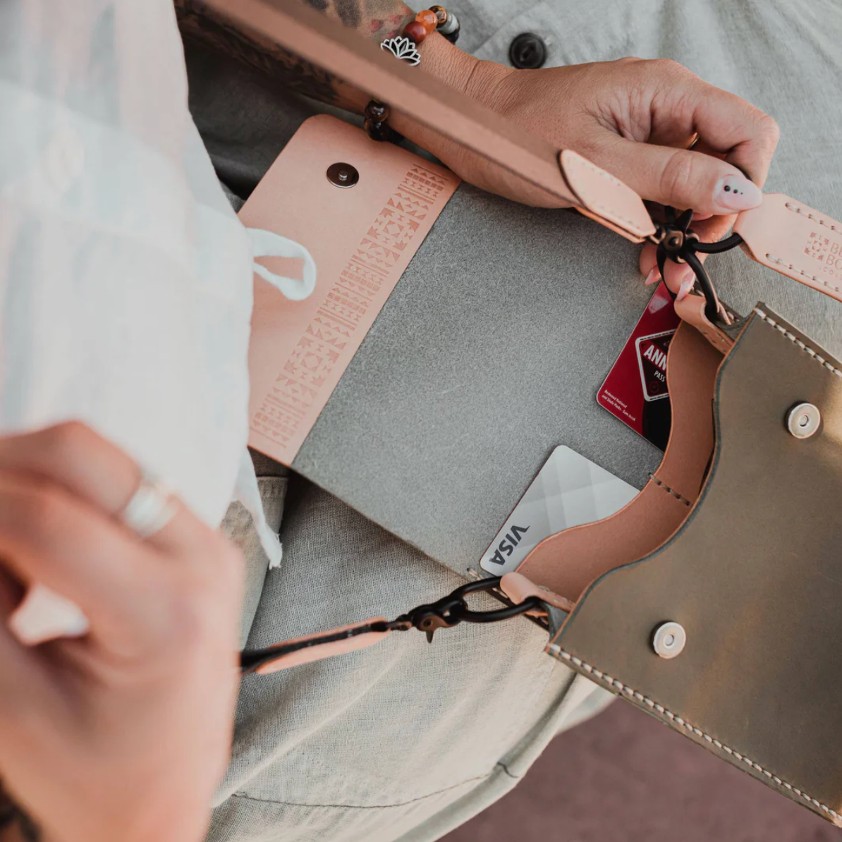 Close-up of hands adjusting a leather strap on a bag with visible brand names.