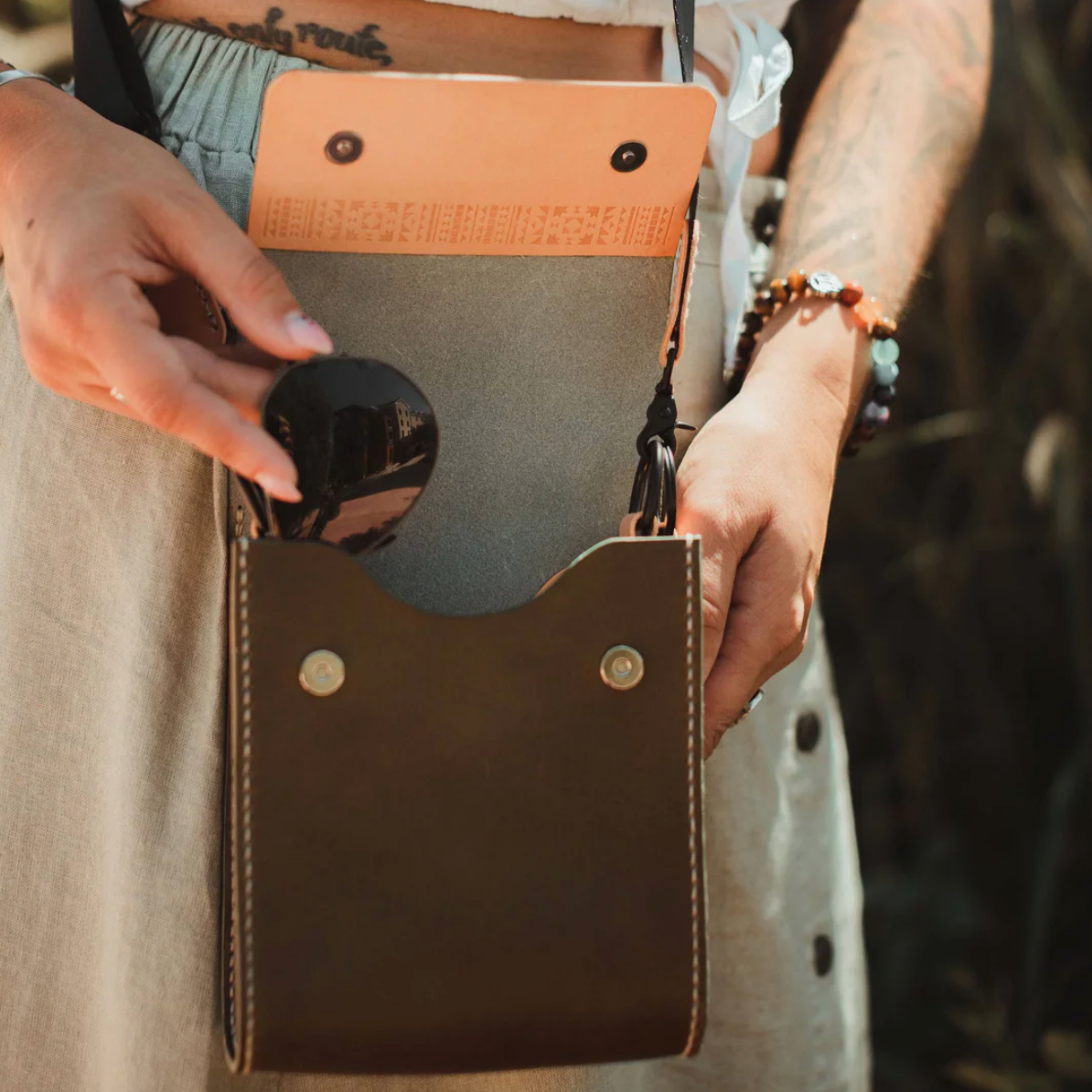Person holding a brown leather pouch with a black object inside, wearing a bracelet.