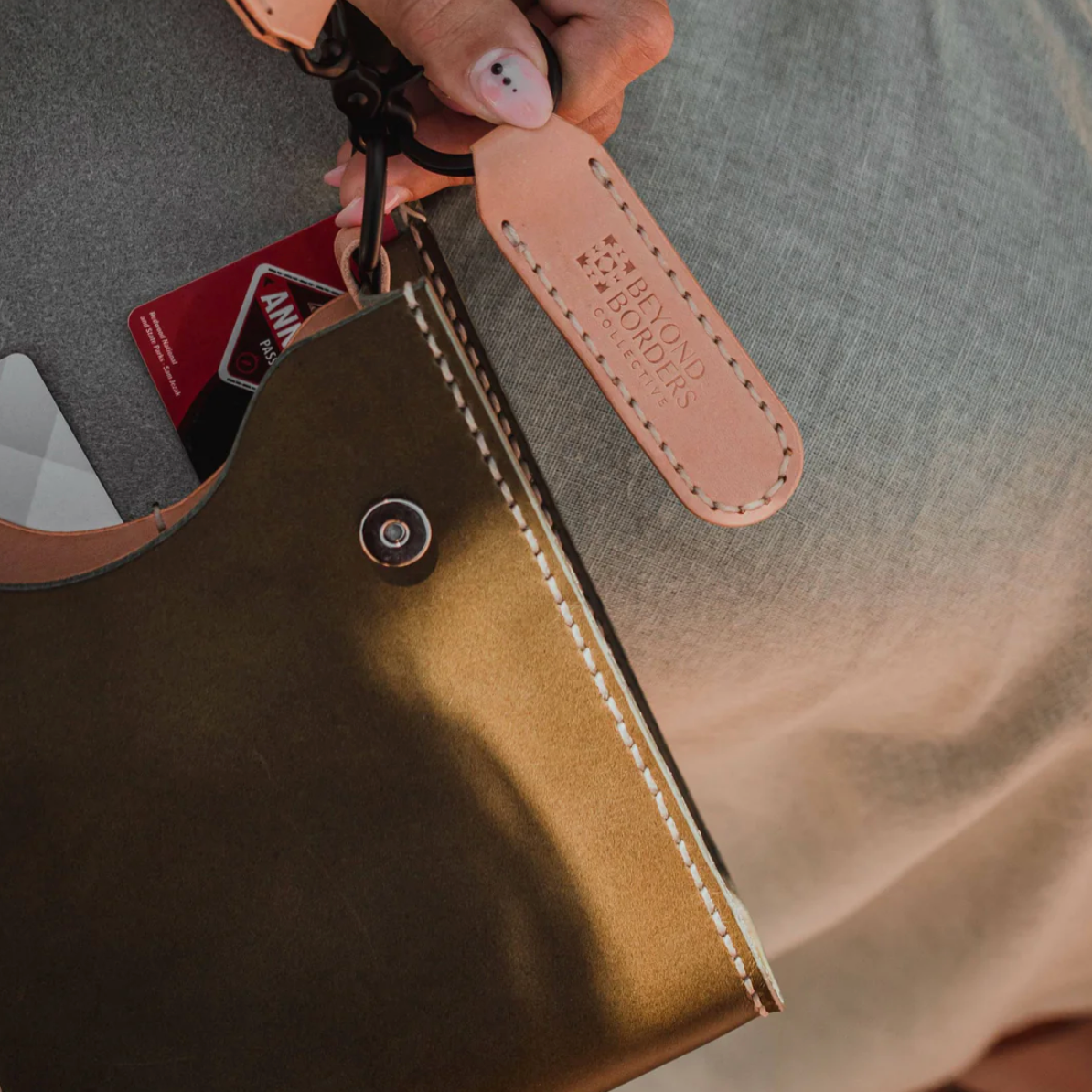 Close-up of a brown leather wallet with a visible brand tag, held against a blurred background.