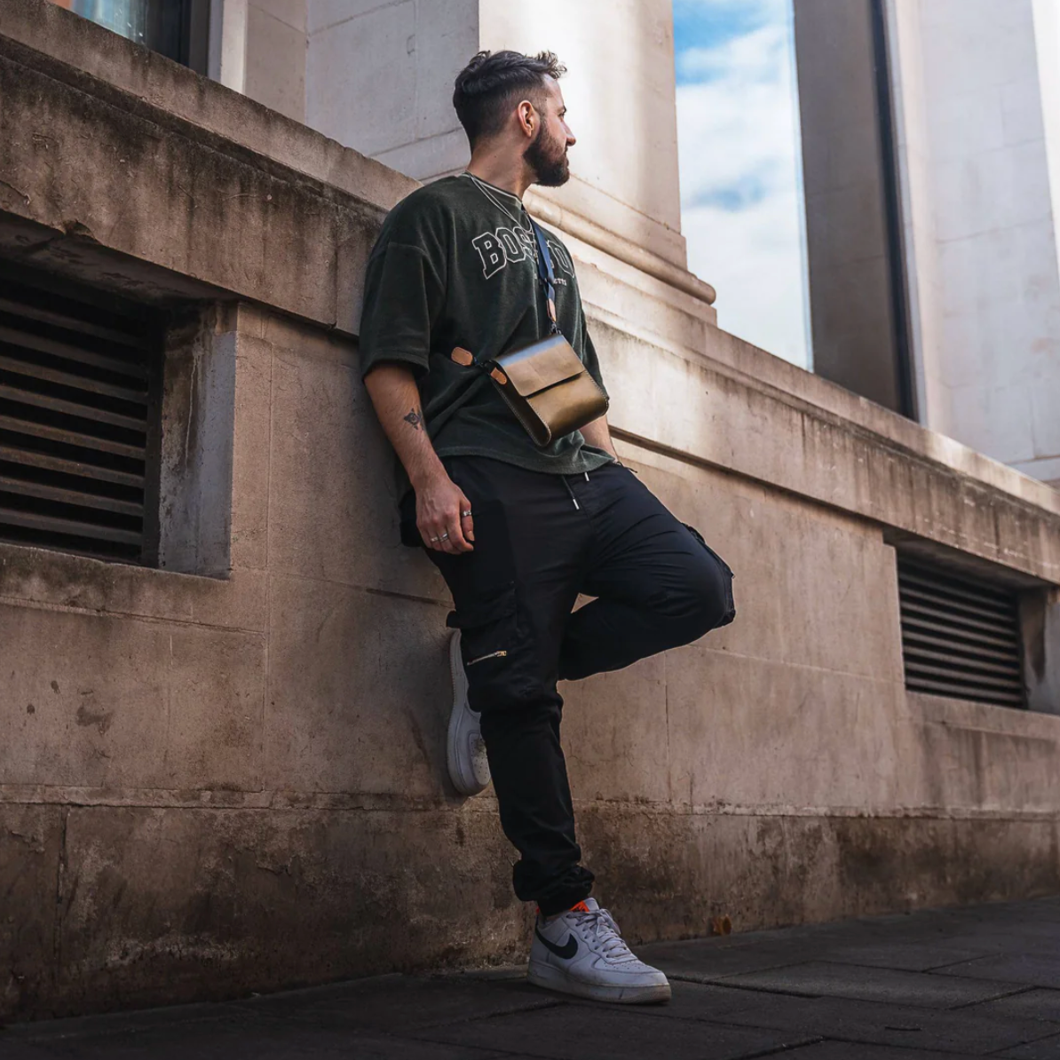 Man leaning against a building wall wearing a green shirt and black pants.