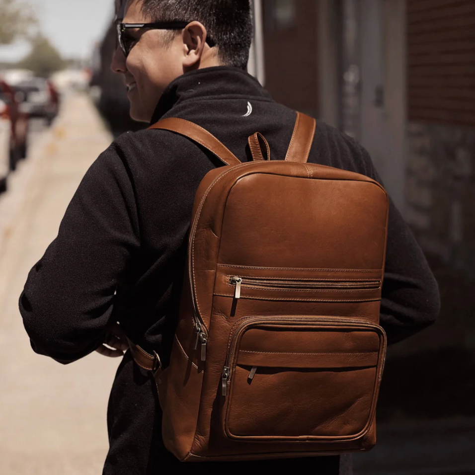 Person wearing a brown leather backpack on a street.