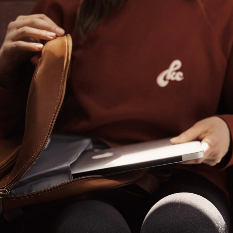Person holding a laptop with a brown jacket featuring a logo.
