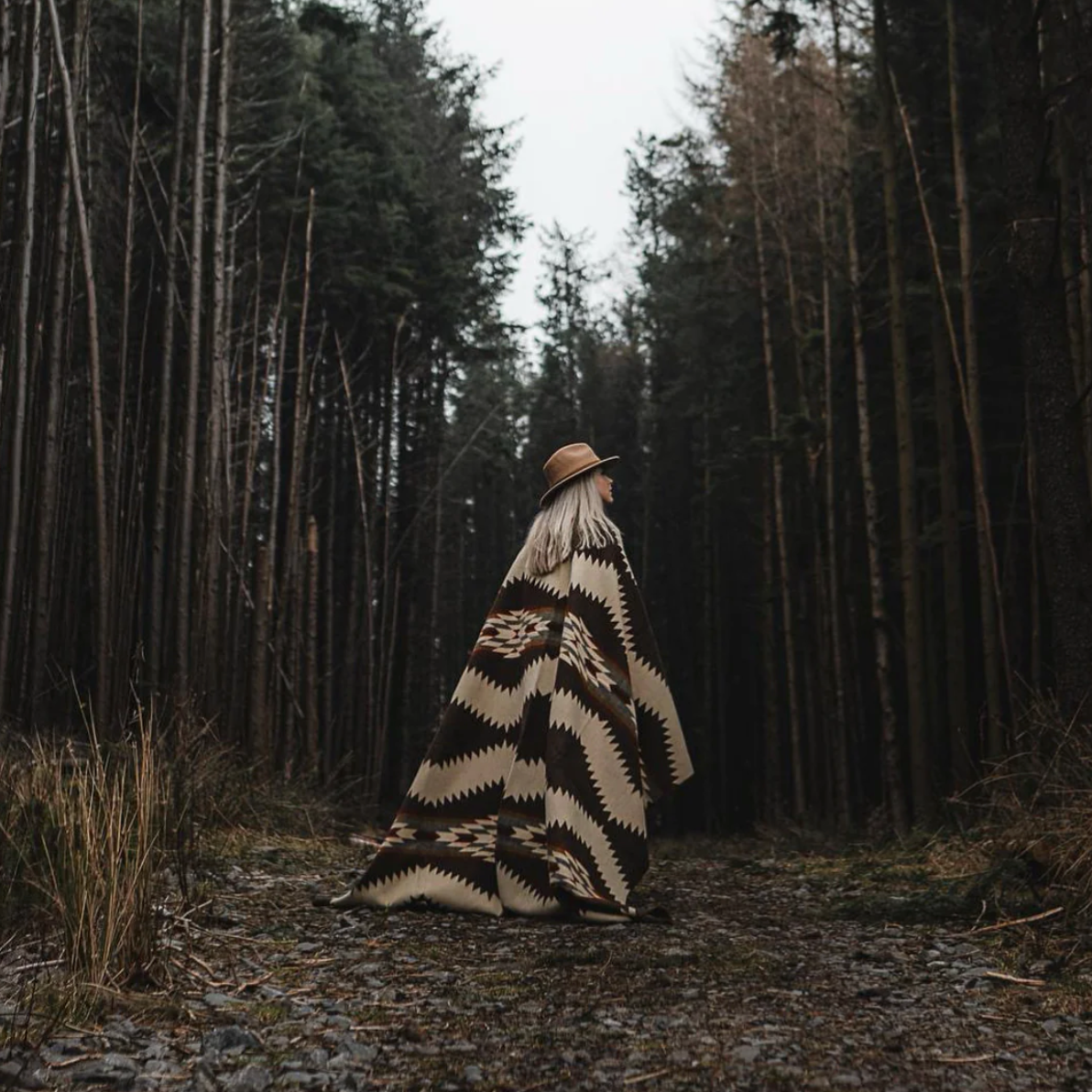 Person wrapped in a patterned blanket walking through a forest