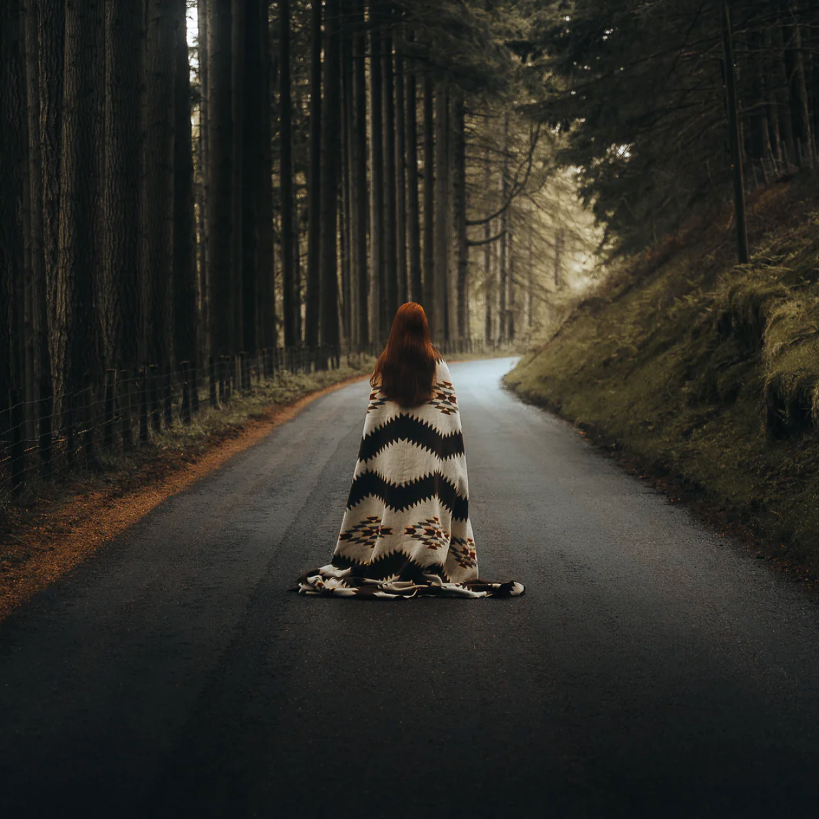 Person wrapped in a patterned blanket standing in the middle of a forest path