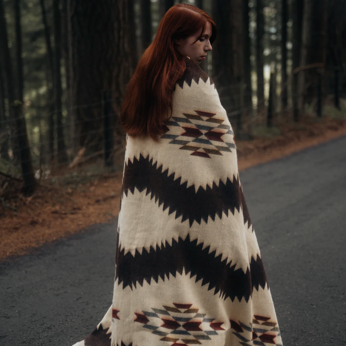 Woman wrapped in a patterned blanket walking on a road in a forest