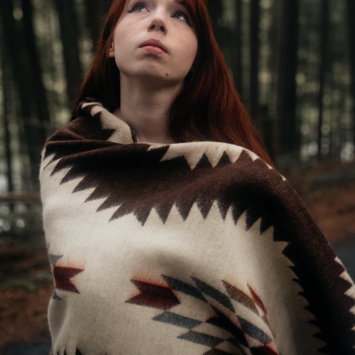 Person wrapped in a patterned blanket in a forest setting