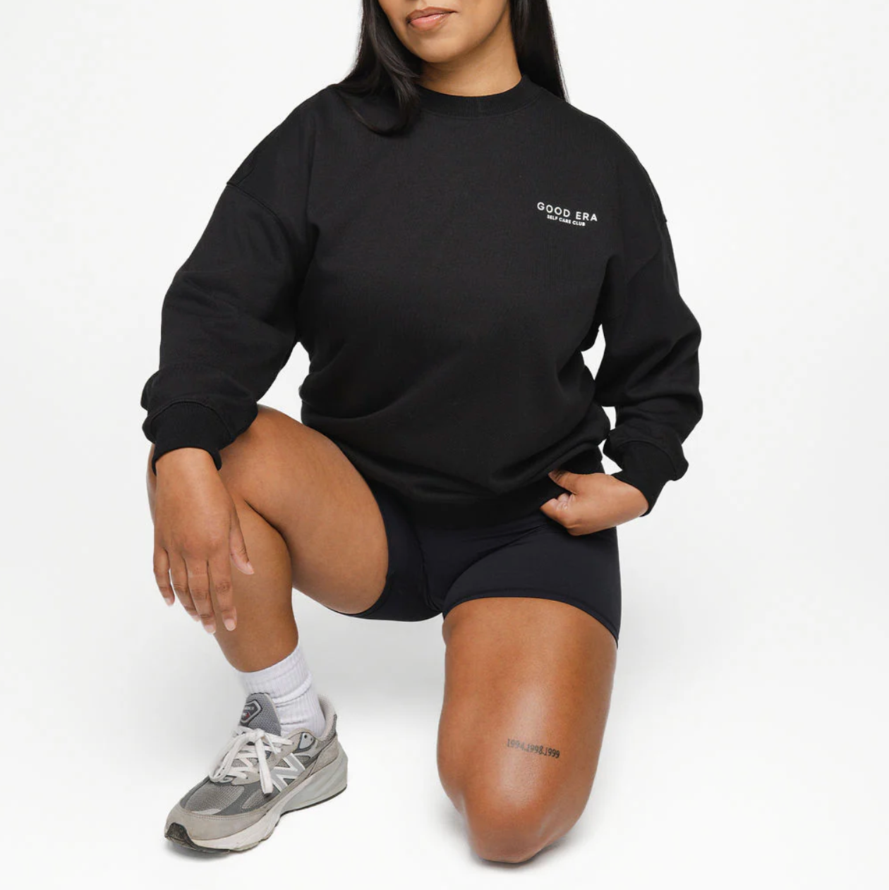Person wearing a black sweatshirt with a logo, sitting on a white background