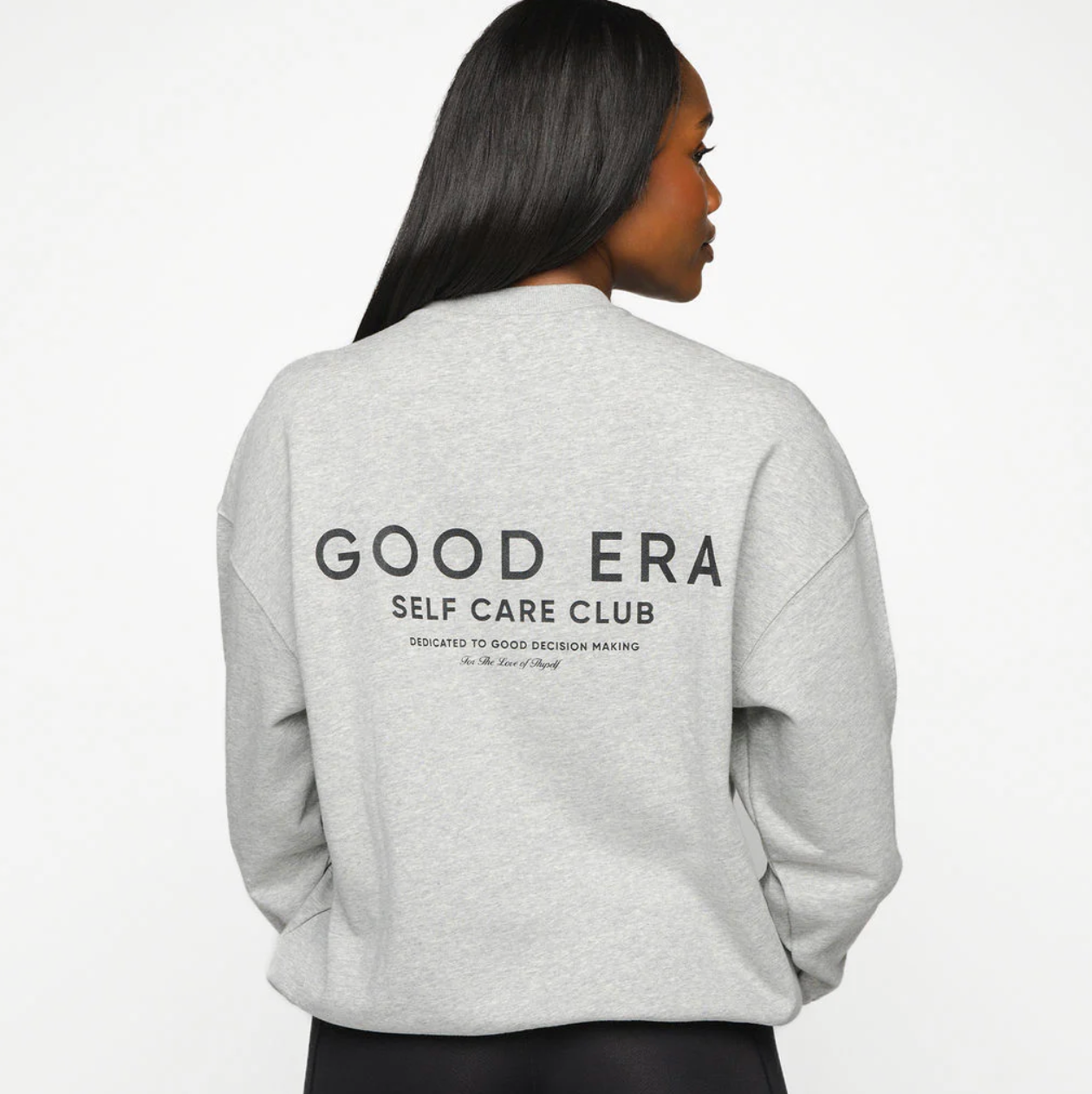Person wearing a gray sweatshirt with 'GOOD ERA SELF CARE CLUB' text on the back against a white background