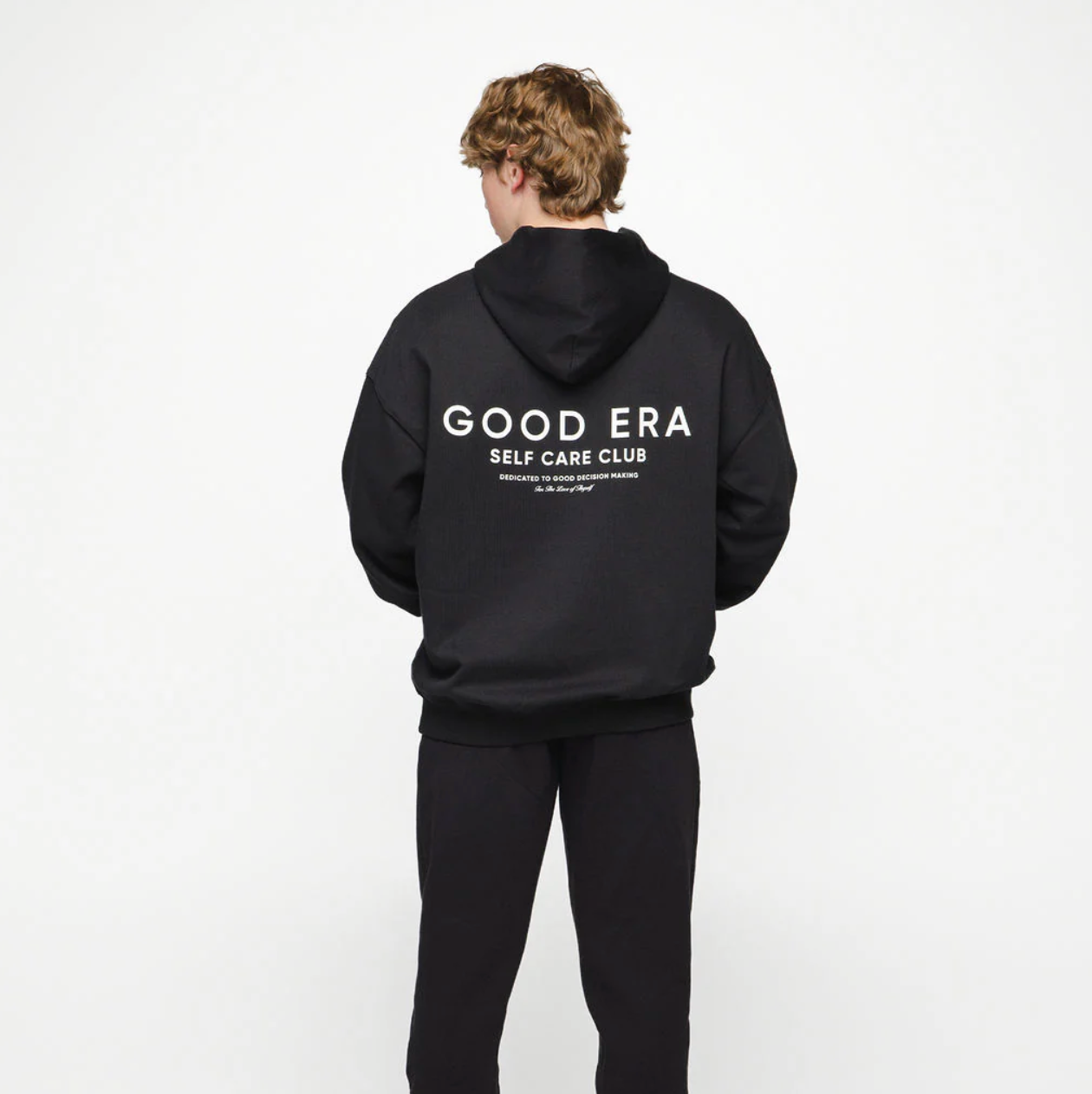 Person wearing a black hoodie with 'GOOD ERA' text on the back against a white background