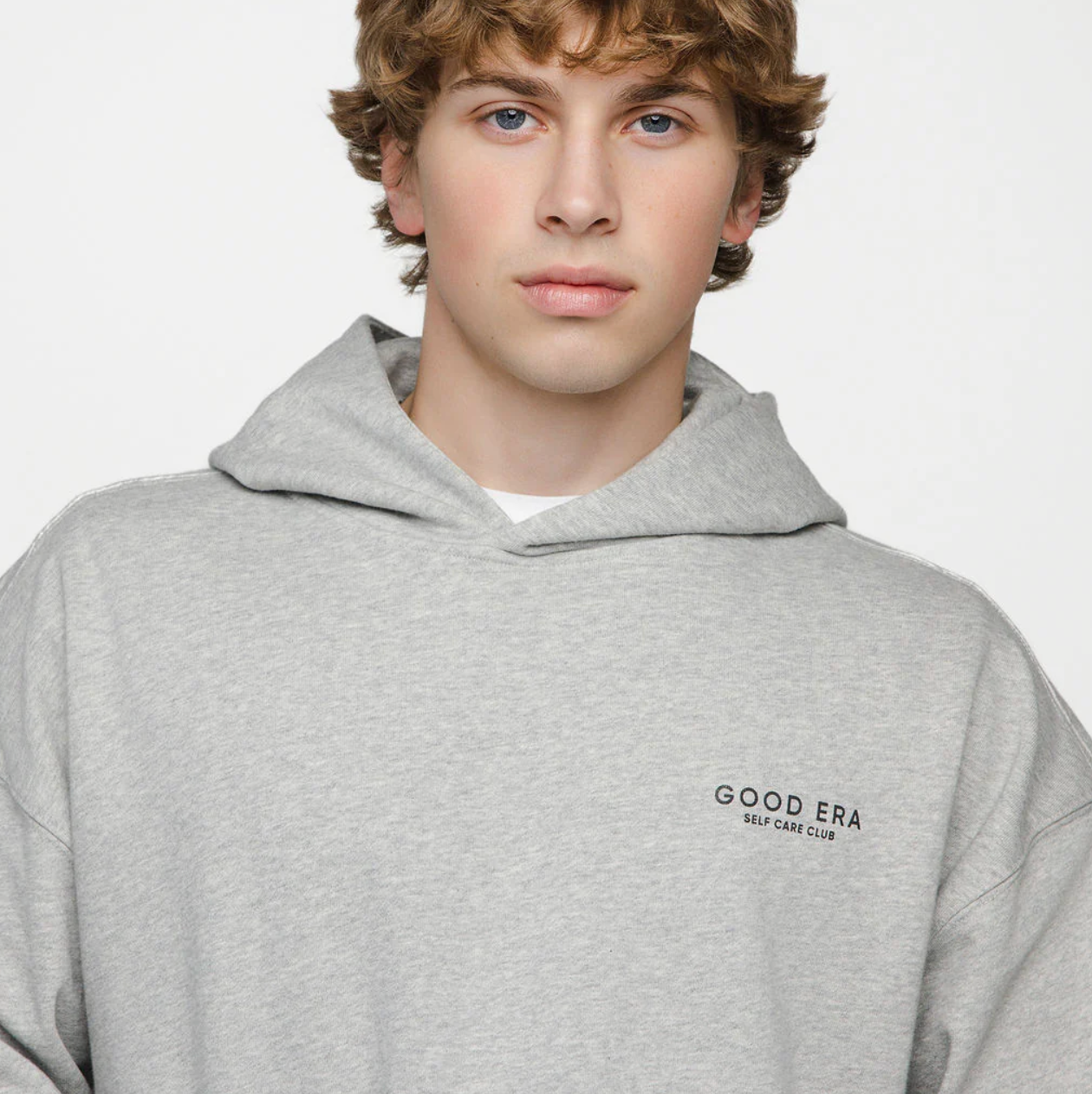 Person wearing a gray hoodie with 'Good Era' logo on a plain background