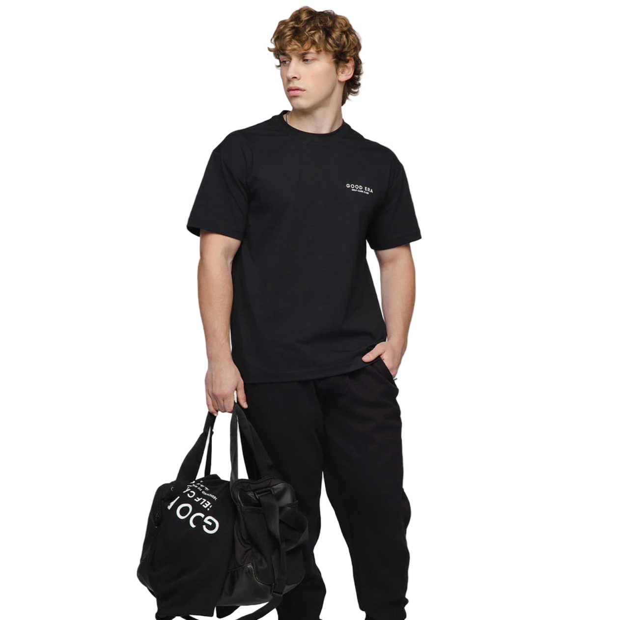 Person wearing a black t-shirt and pants with a logo, holding a black bag on a white background