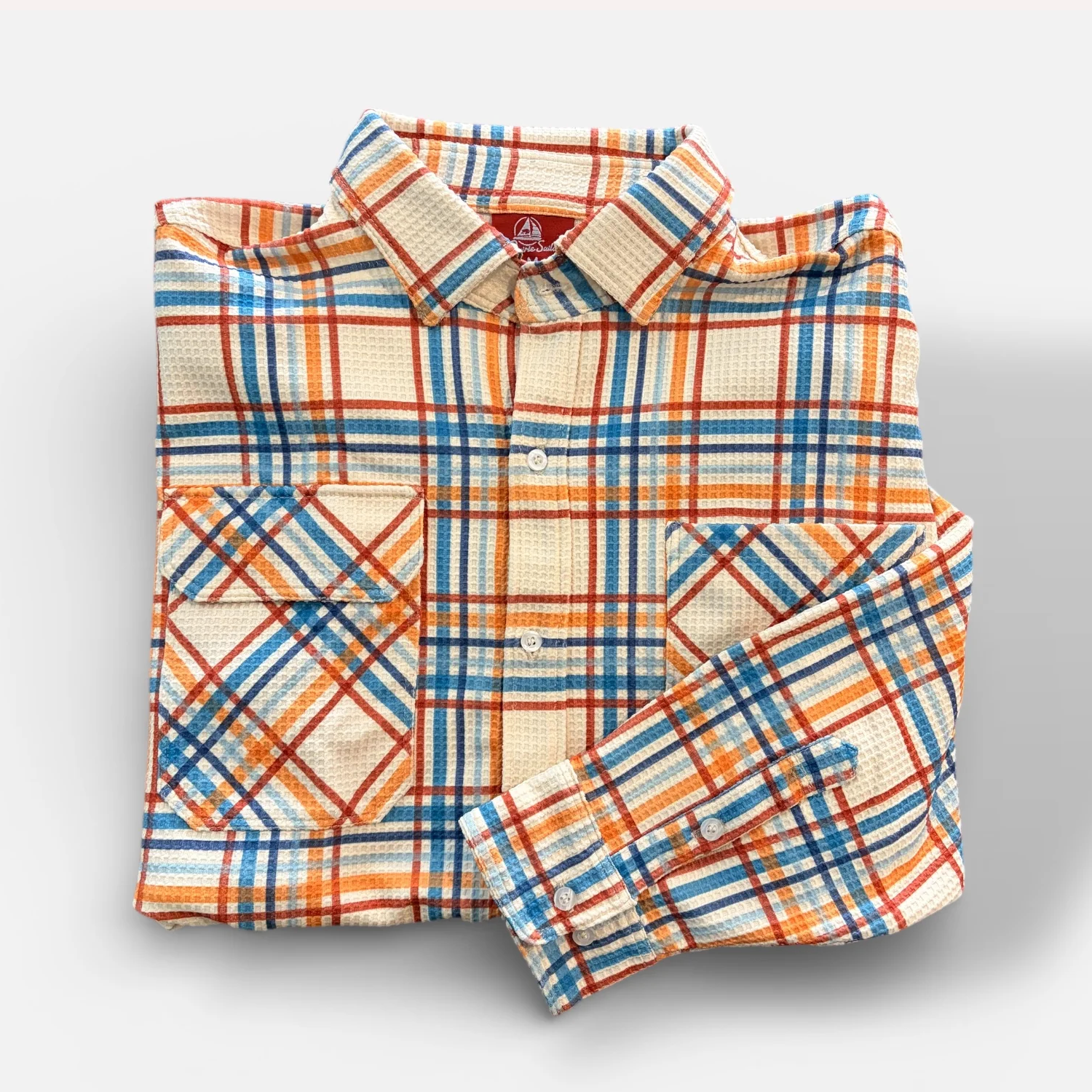 Folded plaid shirt with orange, blue, and beige pattern on a light gray background