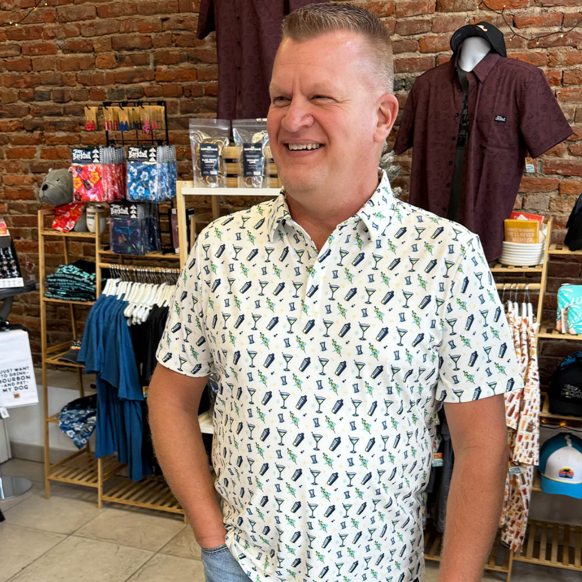 Man wearing a patterned shirt in a store setting with shelves and clothing in the background.