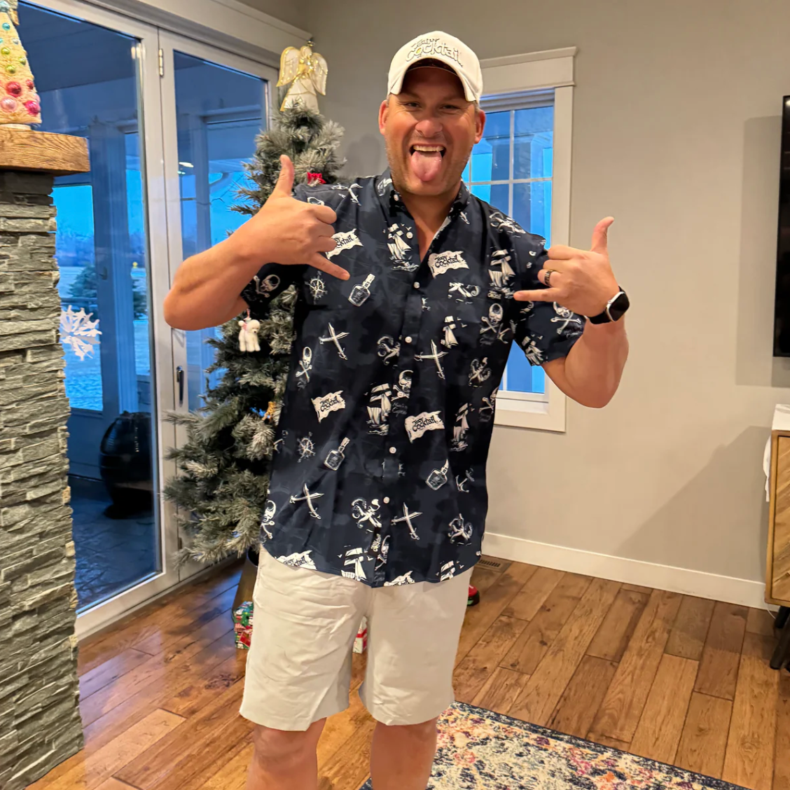 Man giving a double thumbs-up in a room with a Christmas tree and stone wall.