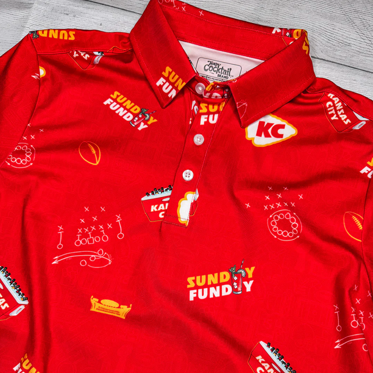 Red polo shirt with various logos and text on a wooden surface