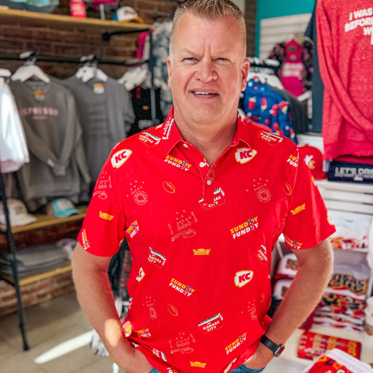 Man wearing a red shirt with various logos in a store setting