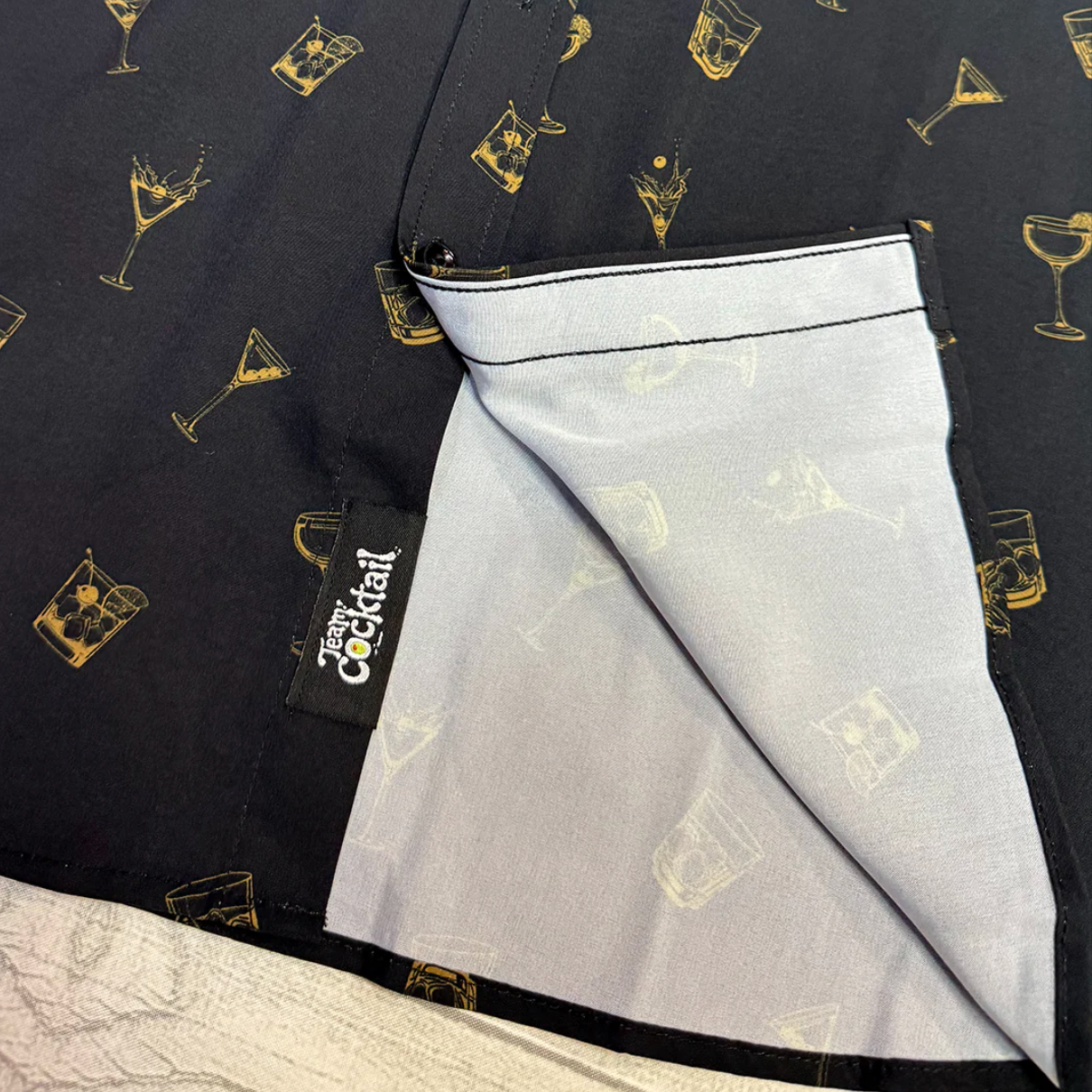 Black shirt with gold cocktail patterns and a white pocket, featuring a 'Team Cocktail' label.
