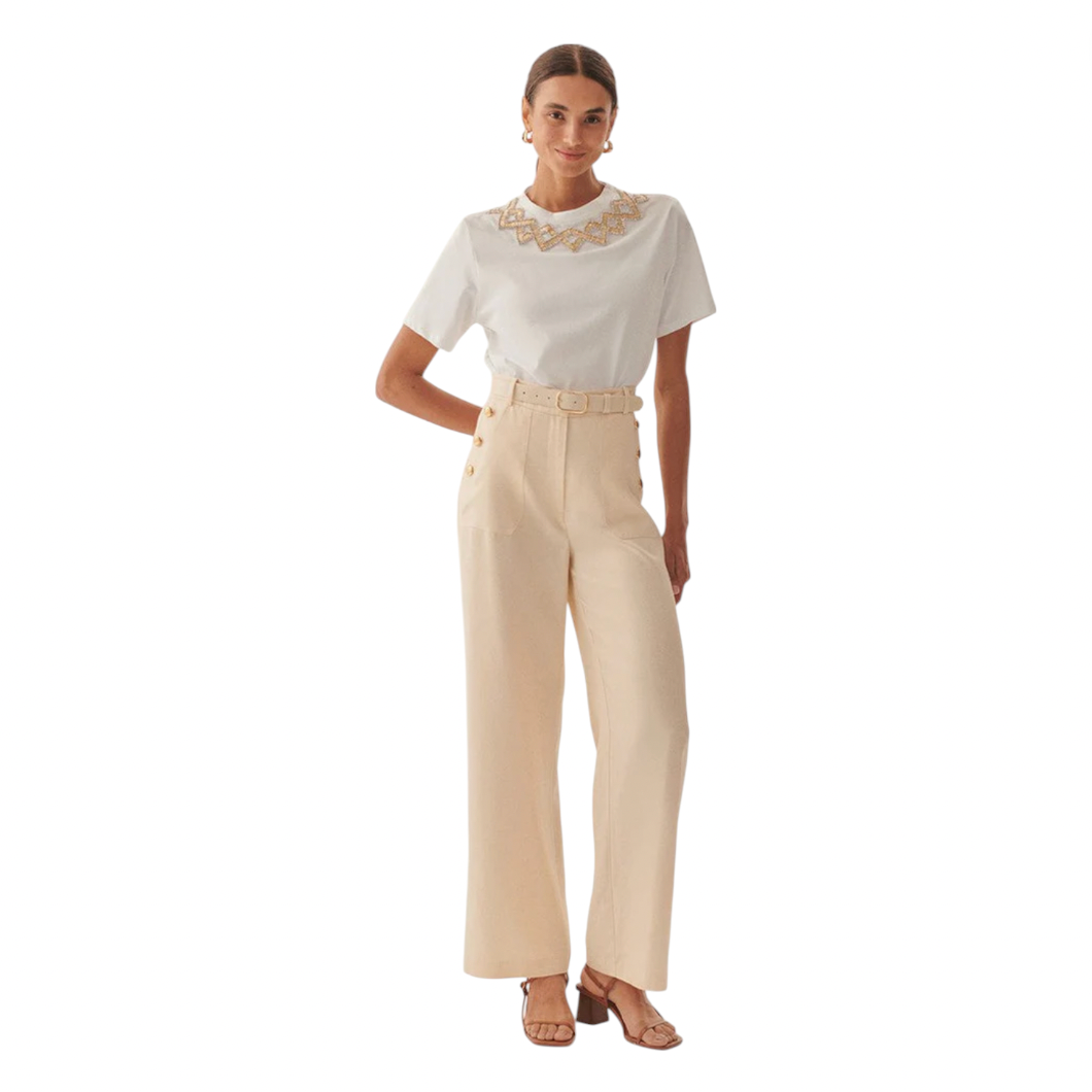 Woman wearing a white blouse with embroidery and beige pants on a white background