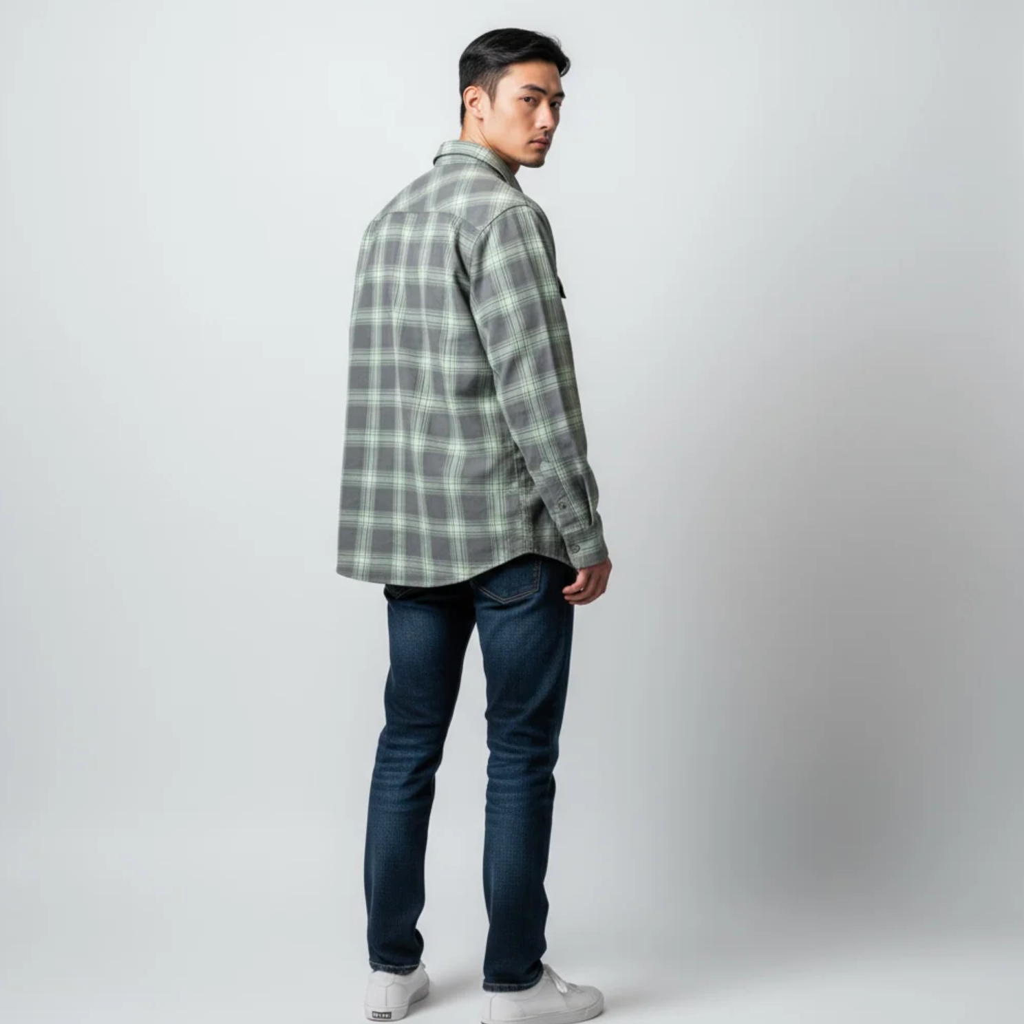 Man wearing a green plaid shirt and dark jeans on a white background