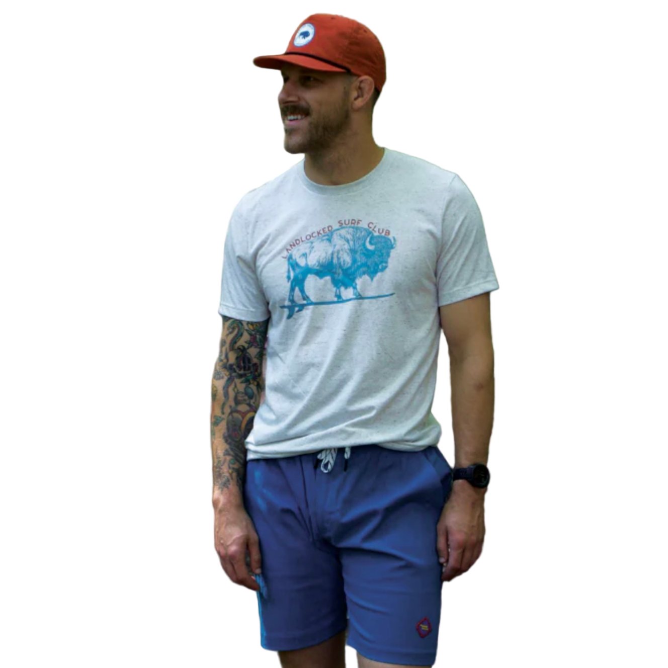 Man wearing a gray t-shirt with a graphic design and blue shorts, standing outdoors with greenery in the background.
