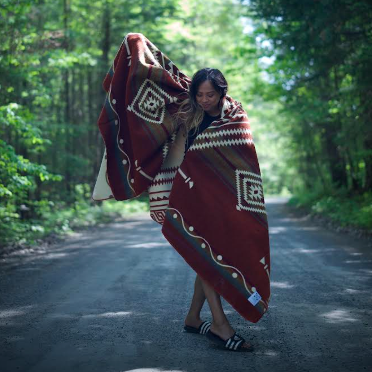Woman wrapped in a patterned blanket standing on a forest path