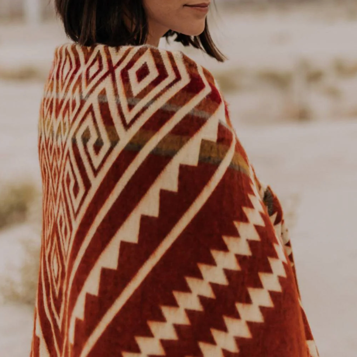 Person wearing a patterned blanket in a desert setting