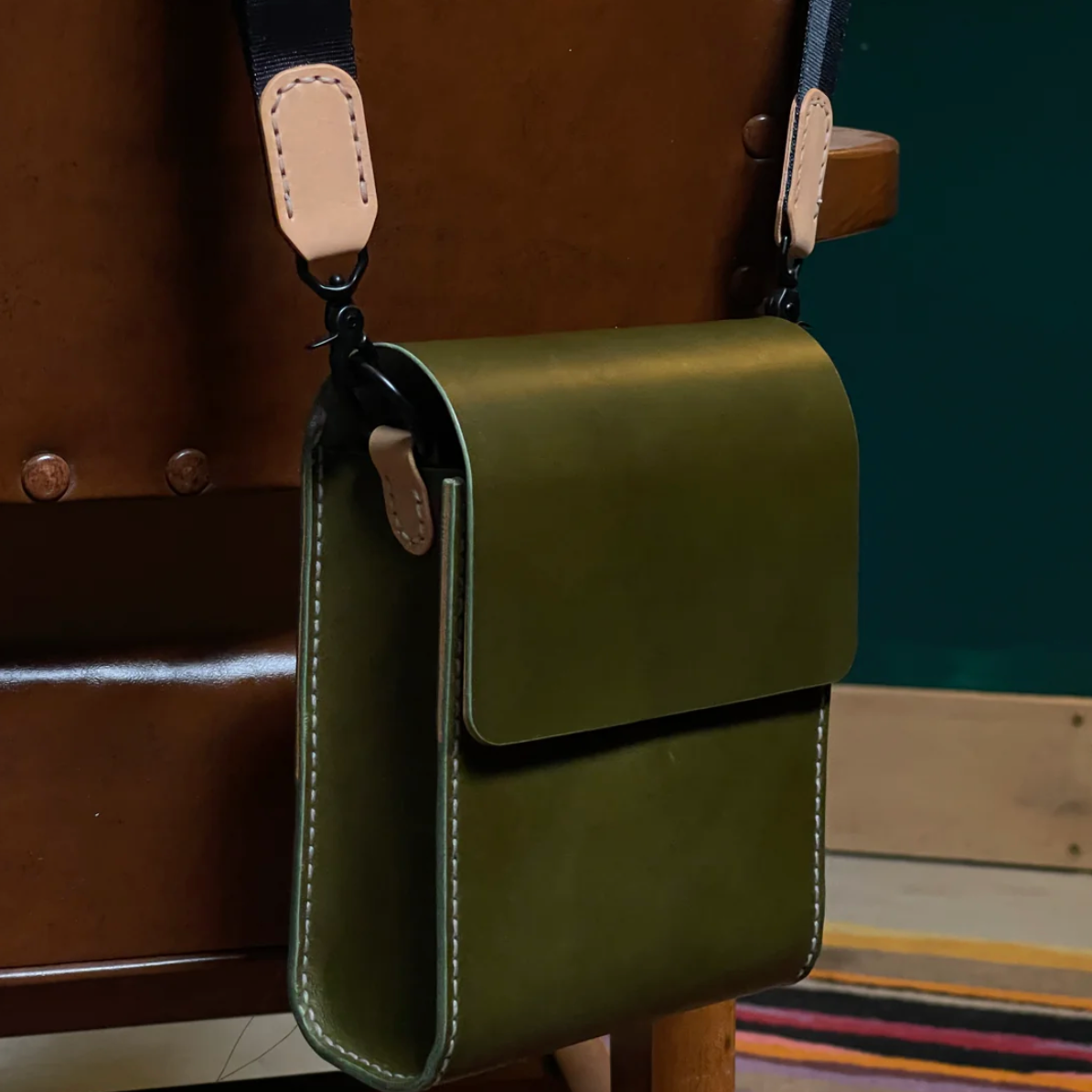 Green leather bag with a strap on a wooden chair