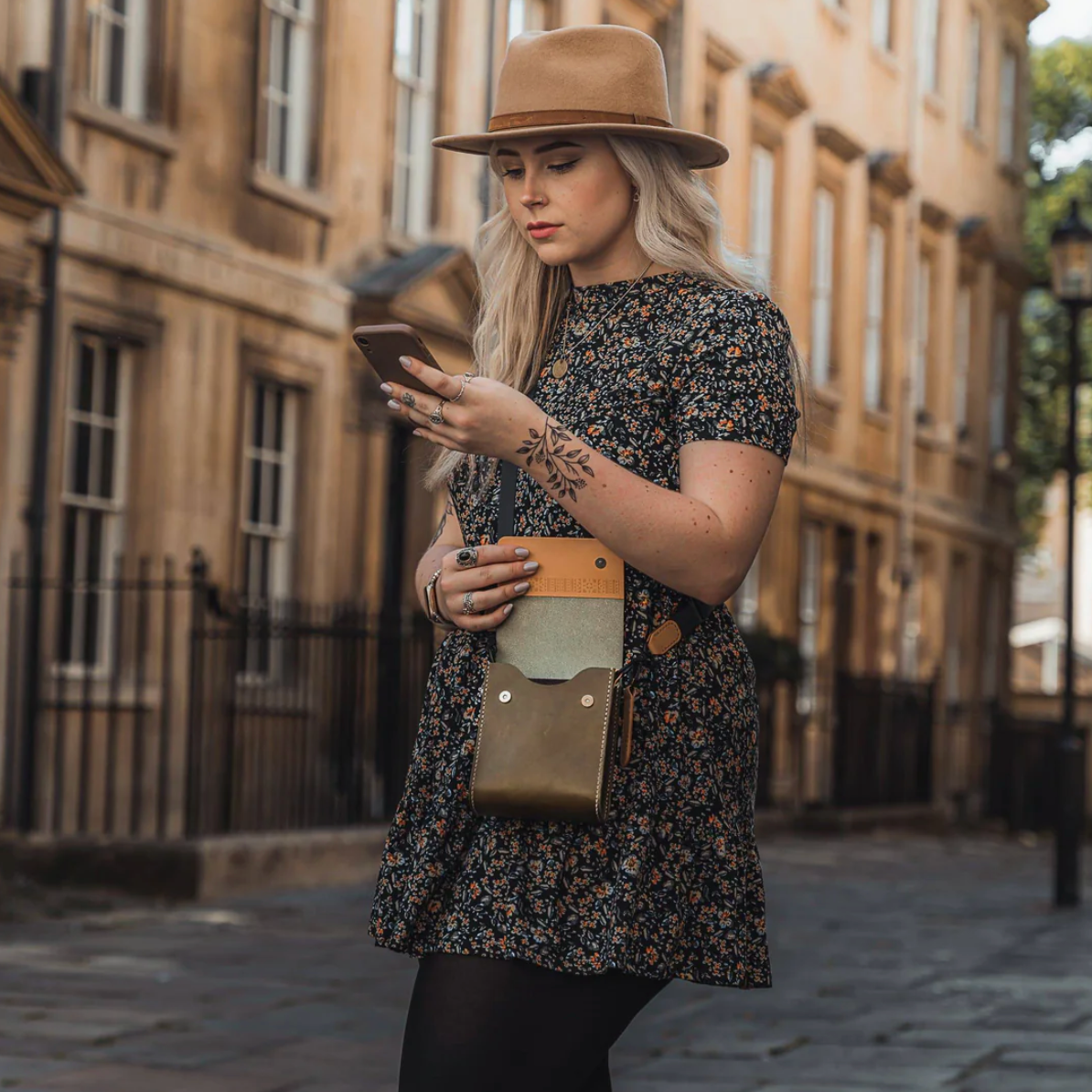 Woman in a floral dress and hat using a phone on a city street.