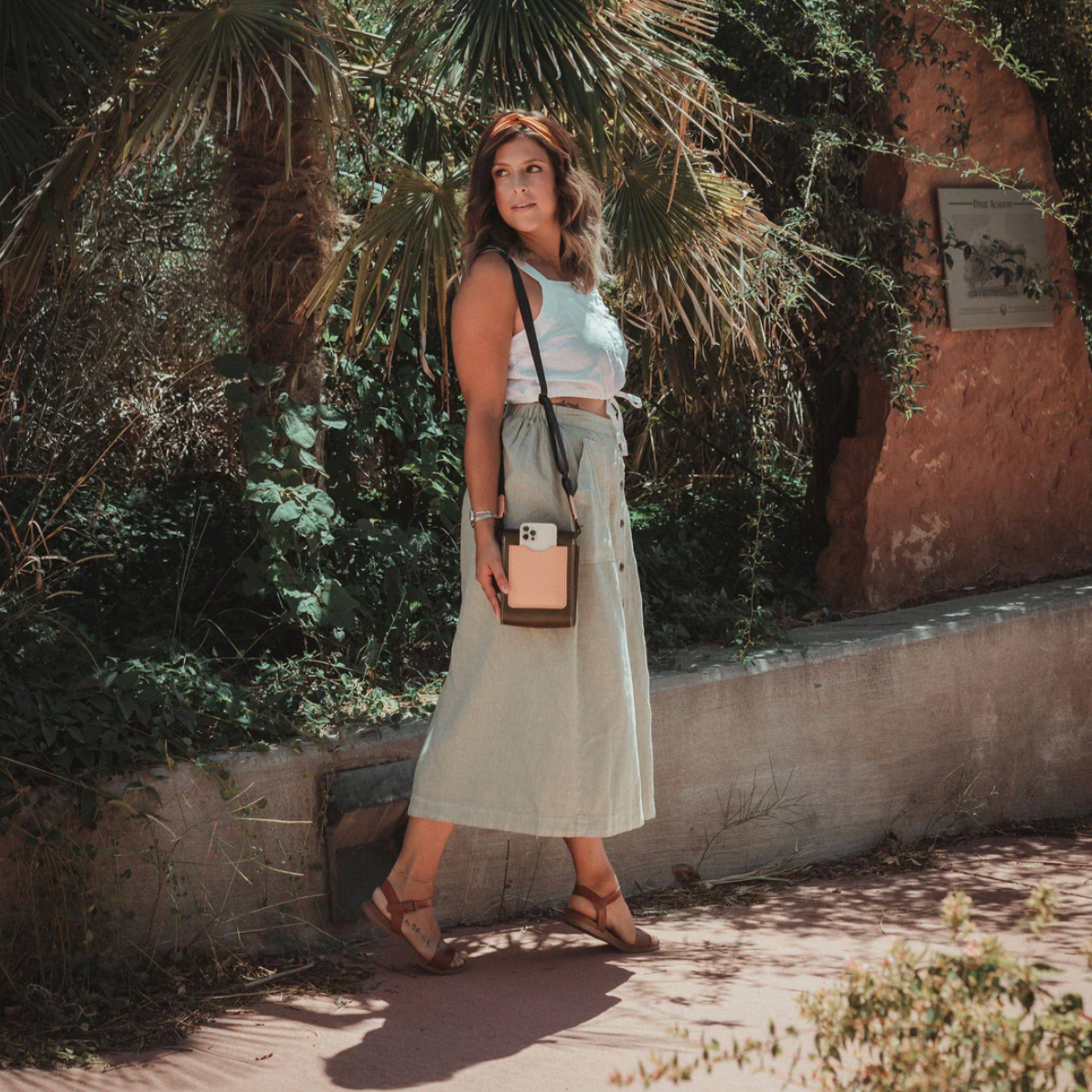 Woman standing outdoors with plants and a wall in the background