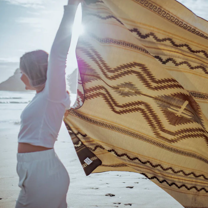 Person holding a patterned fabric with a brand label on a beach