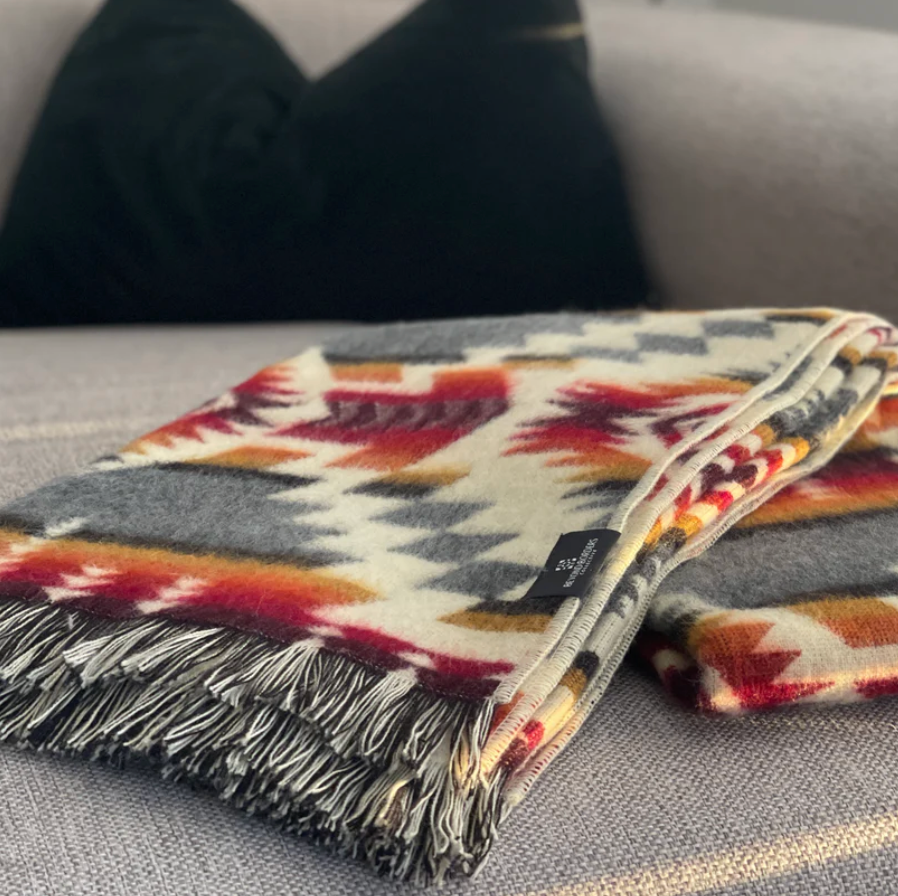 Colorful patterned blanket with fringes on a gray surface