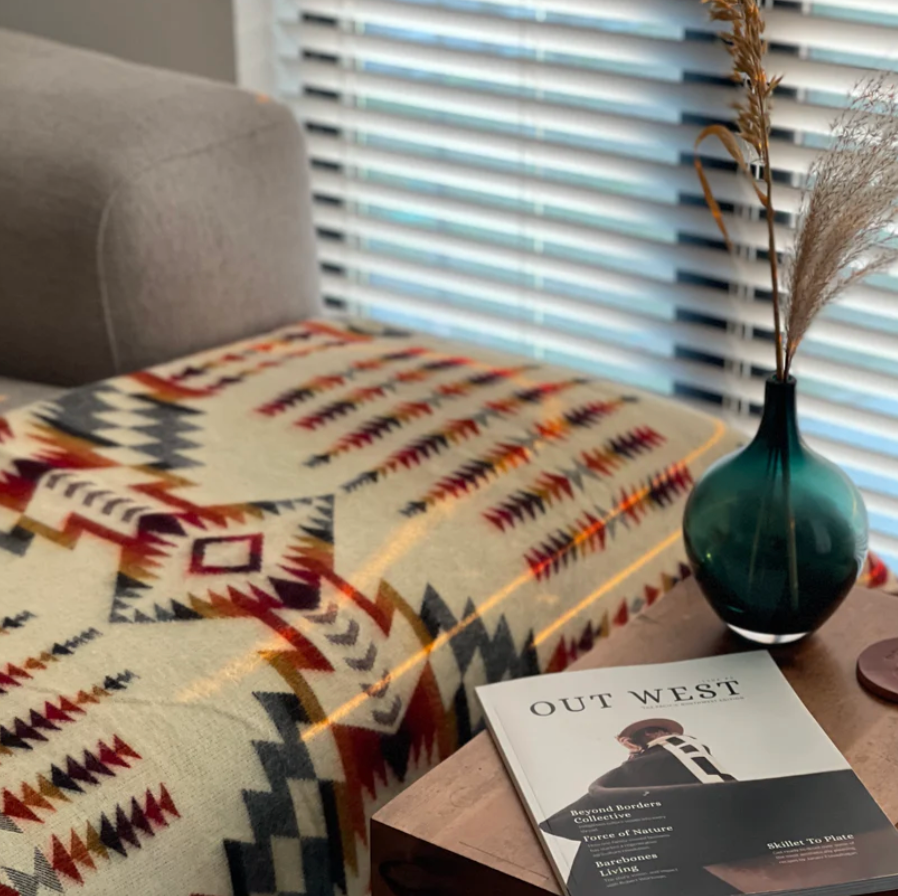 Decorative throw blanket with geometric pattern on a sofa next to a vase and a book titled 'Out West'.