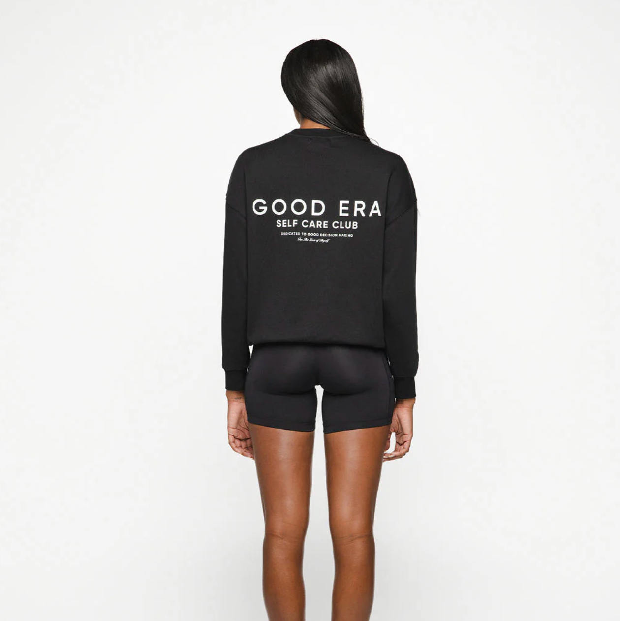 Person wearing a black sweatshirt with 'GOOD ERA SELF CARE CLUB' text on the back against a white background
