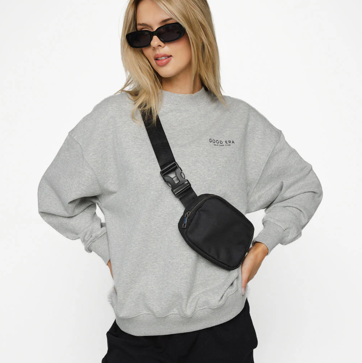 Person wearing a gray sweatshirt with a black bag over one shoulder on a white background