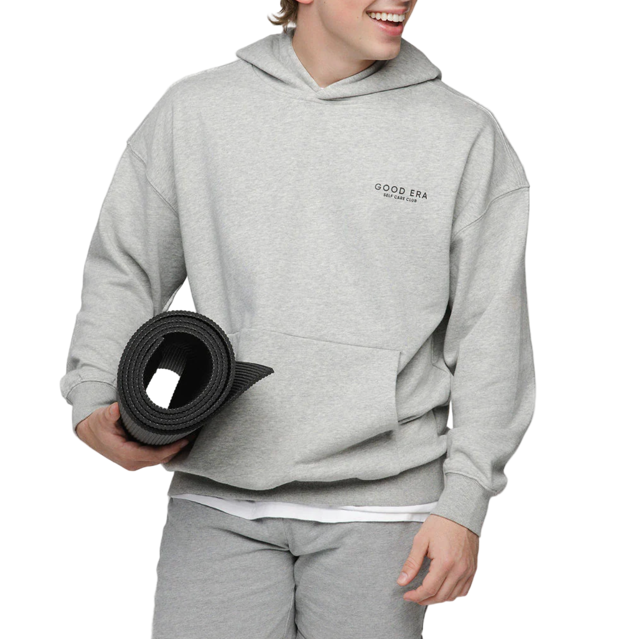 Person wearing a gray 'Good Era' hoodie holding a black yoga mat on a white background