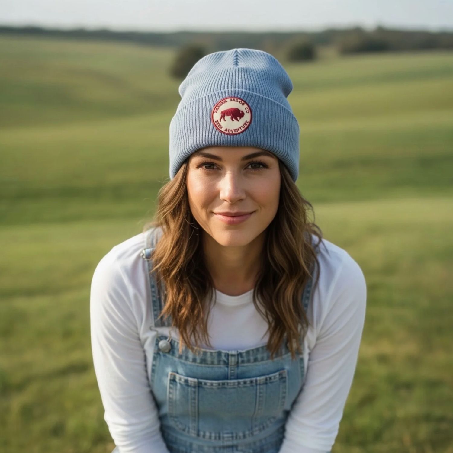 Woman wearing a blue beanie with a logo and denim overalls in a field