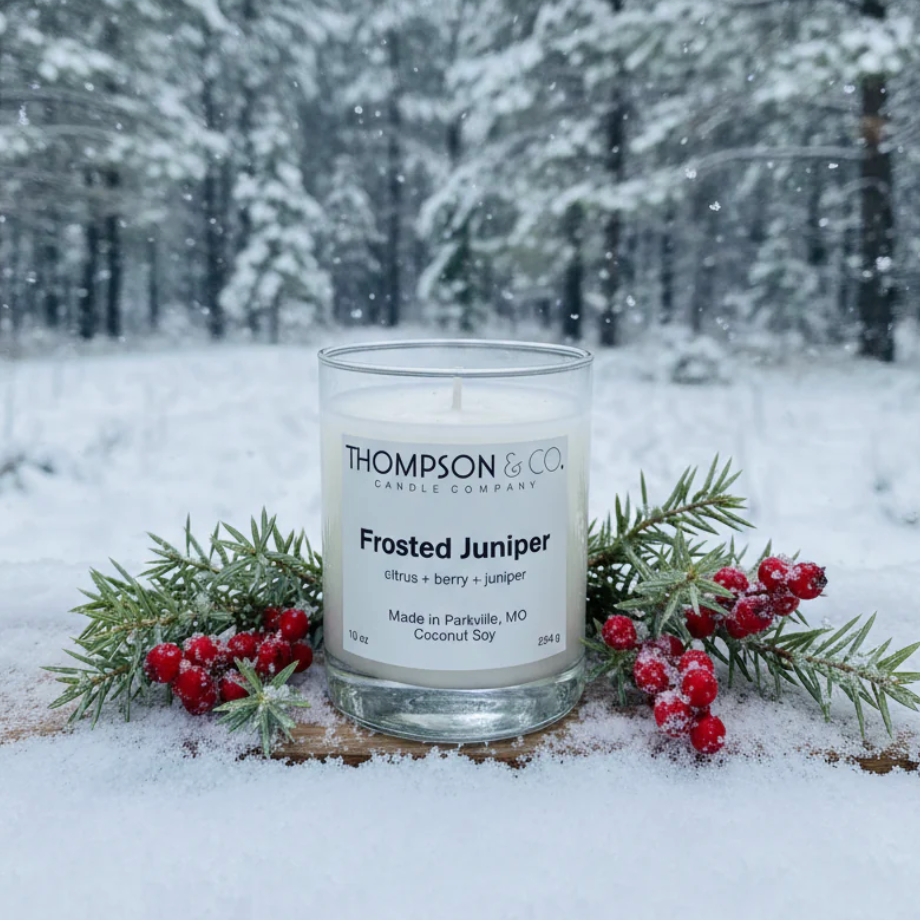 Candle labeled 'Thompson & Co' in a snowy forest setting with berries and evergreen branches.